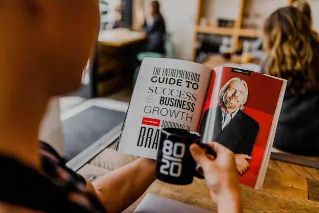 Mann liest einen Ratgeber, in dem ein Foto von Richard Branson abgebildet ist