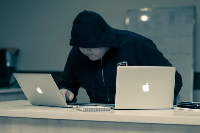 Hacker sitzt vor zwei Laptops