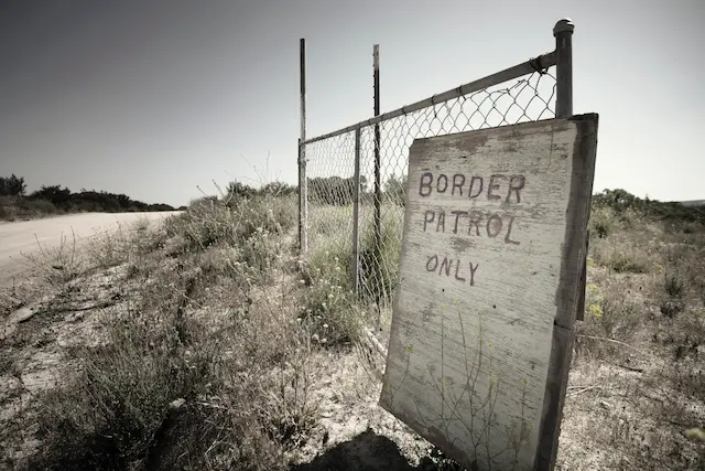 Maschendrahtzaun, an dem ein verwittertes Schild mit der Aufschrift "Border Patrol only" lehnt.