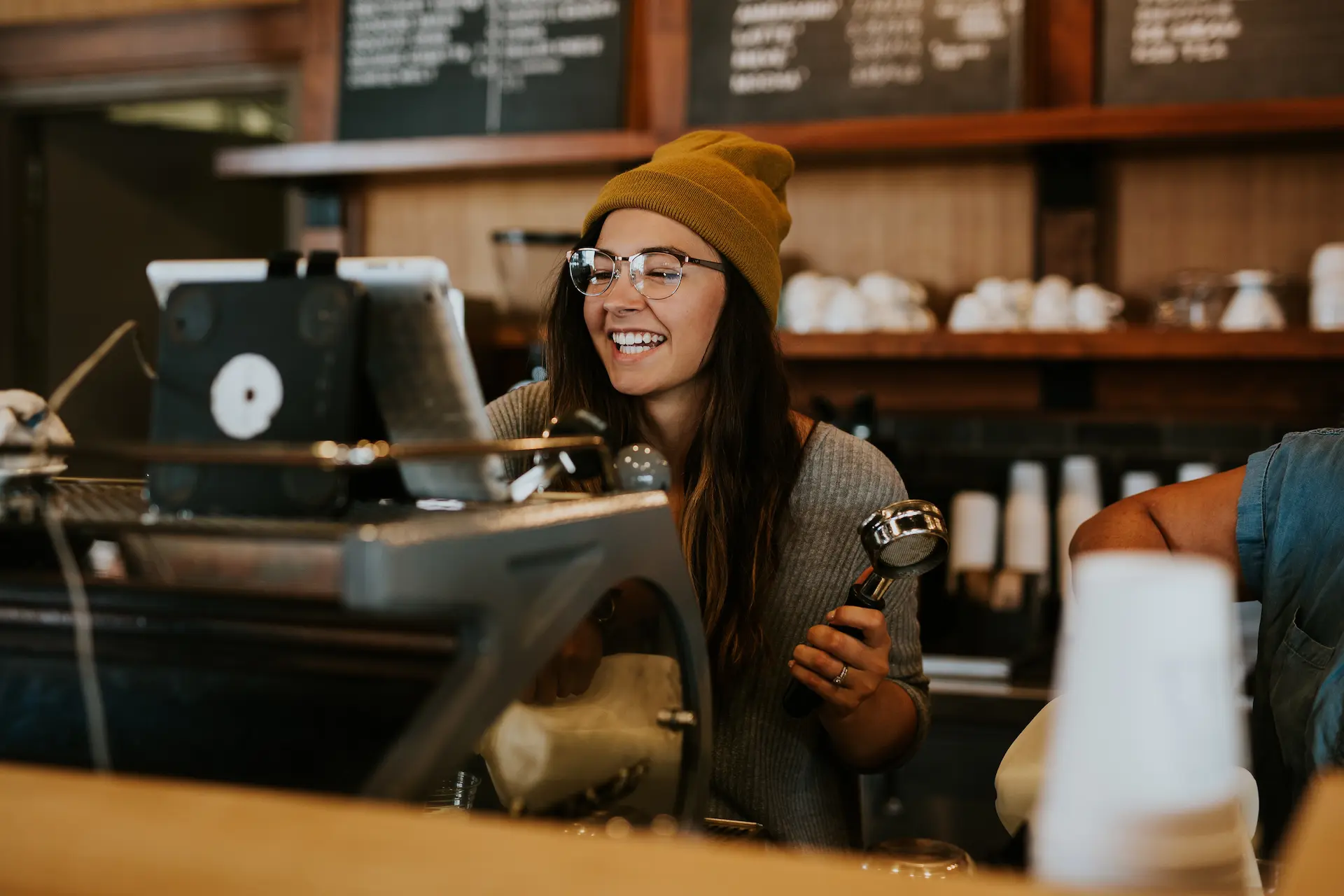 Lachende Barrista arbeitet an der Kaffeemaschine in ihrem Coffee Shop.