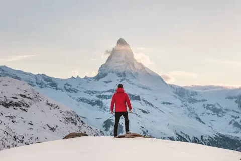 Mann steht auf einem schneebedeckten Berg und schaut zum Gipfel hinauf