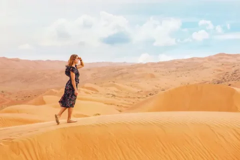 Frau auf einer Sanddüne blickt suchend auf den Horizont