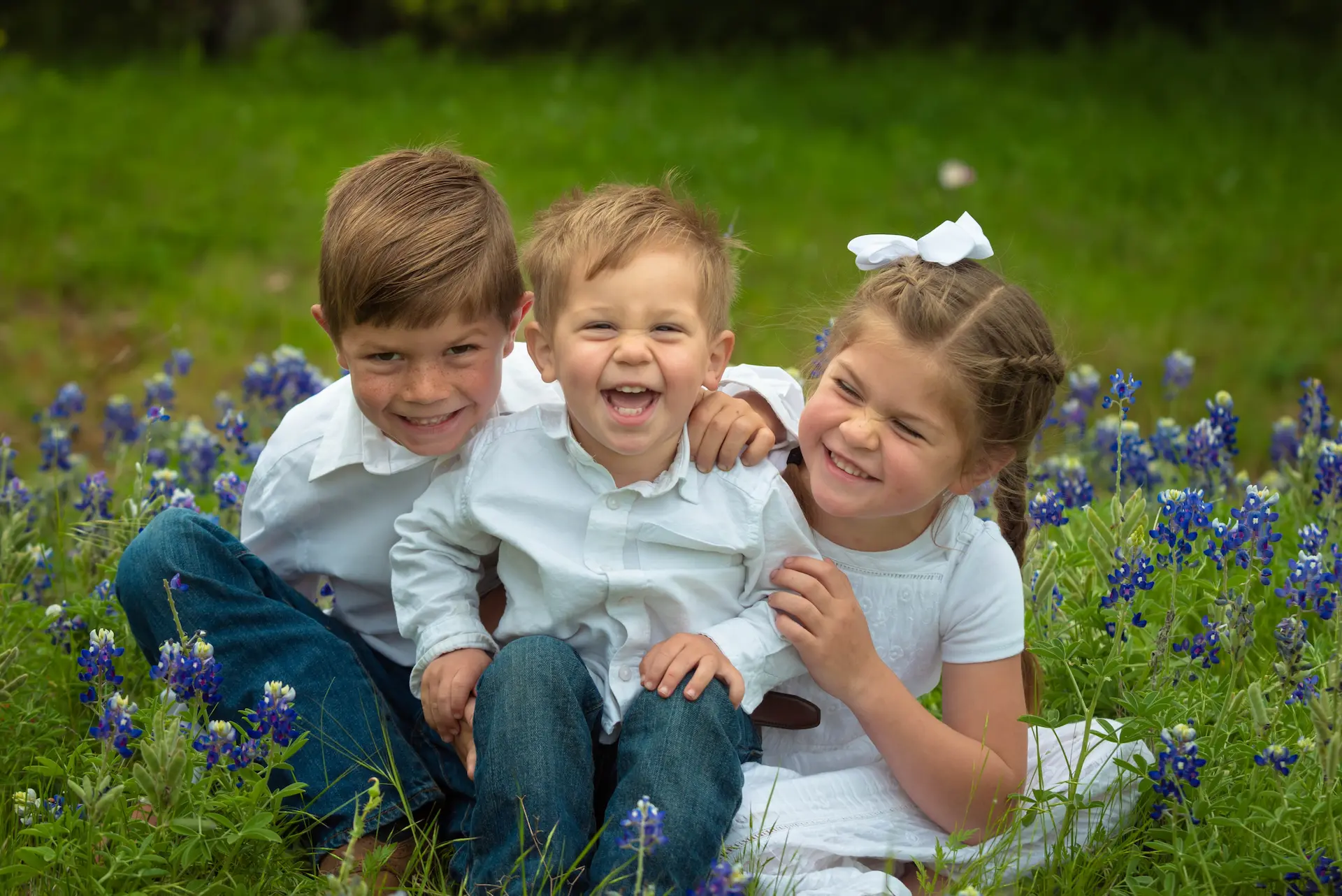 Drei kleine Kinder sitzen auf Blühwiese